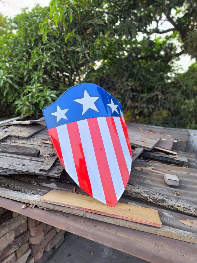 Puede incluir: Un escudo con una parte superior azul con tres estrellas blancas y rayas rojas y blancas. El escudo es un dise&ntilde;o patri&oacute;tico, que recuerda a la bandera estadounidense. El escudo est&aacute; hecho de un material brillante.