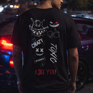 May include: Black t-shirt with white and red graphic designs. The back of the shirt features multiple cartoon faces, the word "CRAZY", the word "TOXIC", and the phrase "I SEE YOU".