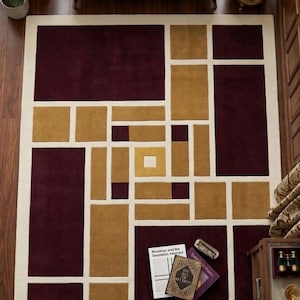 May include: A rectangular area rug featuring a geometric pattern of deep burgundy and mustard yellow blocks separated by thick cream-coloured lines. The design consists of various sized rectangles and squares arranged in a grid-like composition.