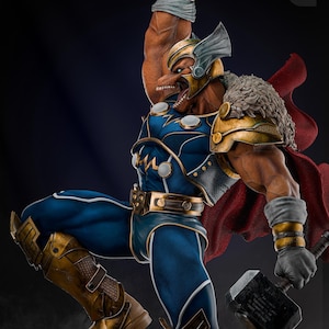 Op de afbeelding: Gedetailleerd beeld van een superheld in een dynamische pose, gekleed in een blauw en goud kostuum met een rode cape. De figuur houdt een hamer vast en draagt een helm. Het beeld heeft een gespierde bouw en staat tegen een donkere achtergrond.