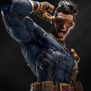May include: A detailed bust of a superhero in a dynamic pose, wearing a blue and gold costume. The figure has a stern expression, with a visor over the eyes and a belt with pouches. The sculpture is set against a dark background.