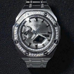 May include: A silver G-Shock Casio watch with a diamond-encrusted bezel and band. The watch face is gray with black hands and a digital display showing the number 39. The watch has a stainless steel band.