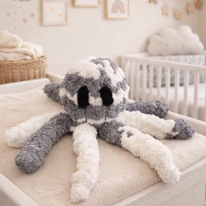 May include: A handmade plush octopus toy in shades of grey and white, with black eyes. The soft toy is designed with a textured, fluffy material and is placed on a neutral-coloured surface, suggesting a nursery or children's room setting.