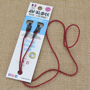 Peut inclure: Un cordon rouge avec un fermoir noir et une étiquette de produit blanche et bleue. L'étiquette contient du texte français, dont "AV BLOCK" et "Serrez... c'est bloqué !". Le cordon est fait d'un matériau tissé.