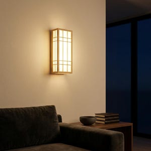 May include: A rectangular wooden wall sconce with a grid design, emitting a warm, inviting light. The fixture is mounted on a neutral-colored wall, creating a soft glow in the room. The design is reminiscent of Japanese style.