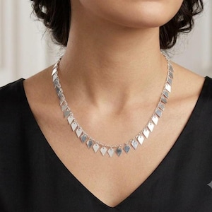 May include: A silver-toned necklace featuring a delicate chain adorned with numerous small, flat, diamond-shaped metal charms hanging at regular intervals along the entire length of the chain, creating a uniform and repetitive pattern.