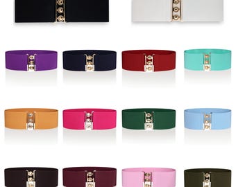 May include: A collection of colorful elastic belts with gold-tone clasps. The belts come in various colors, including black, white, purple, navy, red, teal, tan, pink, green, and light blue. Each belt has a wide, stretchy band.