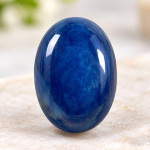 Op de afbeelding: Een gepolijste, ovaalvormige blauwe edelsteen met een glad, in cabochon geslepen oppervlak. De steen vertoont een diepe, verzadigde koningsblauwe kleur met subtiele interne variaties en een reflecterende, glanzende afwerking.