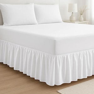 May include: A white bed featuring a white fitted sheet, two white pillows, and a white bed skirt with a ruffled design. The image highlights bedroom textiles and bedding, emphasizing a clean aesthetic.