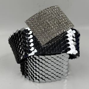 May include: A silver bracelet featuring a square, crystal-studded centrepiece. The bracelet is constructed from overlapping, scale-shaped metal elements. A striking accessory, ideal for evening wear or special events.