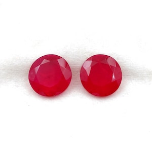 Puede incluir: Dos gemas redondas, facetadas, de color rojo brillante. Las gemas se muestran sobre un fondo blanco. Las gemas tienen un alto brillo y parecen ser de alta calidad. Las gemas son probablemente rubíes o piedras preciosas similares.