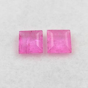 May include: Two square-cut, faceted pink gemstones. The gems have a vibrant, translucent colour and are set against a white background. The facets create a play of light and shadow, enhancing their brilliance. These gemstones are suitable for jewellery making.