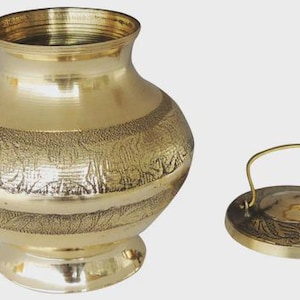 Puede incluir: Una olla de metal dorado con tapa. La olla tiene un cuerpo redondeado con diseños florales grabados y una abertura ancha. La tapa es redonda con un asa. La olla se asienta sobre una base pequeña y redonda.