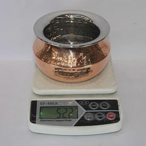 Puede incluir: Una taza de cerámica blanca con un asa negra y el texto "But First, Coffee" en un estilo manuscrito. La taza está sobre una superficie blanca. La taza mide aproximadamente 10 cm de alto.