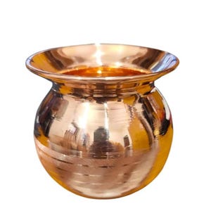 May include: A shiny copper-colored pot with a wide, flared rim and a rounded body. The pot has a smooth, reflective surface with horizontal etched lines around the middle. The interior of the pot is a darker copper color.