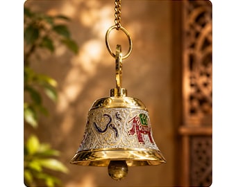 May include: A polished brass hanging bell featuring an intricate silver-toned embossed pattern. The design includes a colorful elephant motif with red and green accents, a prominent Om symbol, and a metal chain attached to a circular top ring.