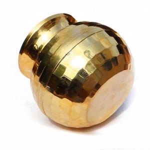 May include: A golden, hammered-metal pot with a wide, flared rim. The pot has a rounded body and a textured surface, reflecting light. The overall design is simple and elegant, suitable for decorative purposes.