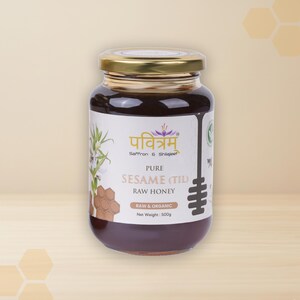 Op de afbeelding: Een pot rauwe sesam honing met een gouden deksel. Het etiket bevat tekst in meerdere talen, waaronder "PURE SESAME (TIL) RAW HONEY" en "RAW & ORGANIC". De pot bevat 500g honing.
