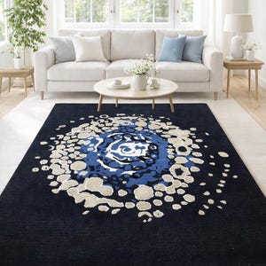 May include: A navy blue area rug with a large, abstract floral design in shades of blue and beige. The rug is placed in a living room setting, with a white sofa, coffee table, and natural light.
