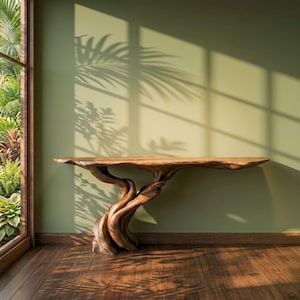 Puede incluir: Una consola de madera hecha a mano con un diseño natural y orgánico. La mesa presenta una tapa de borde vivo y una base de madera esculpida y entrelazada, creando una pieza artística única. La mesa está colocada contra una pared verde con sombras.