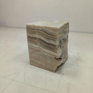 May include: A rectangular, natural stone side table. The table is a light beige colour with horizontal bands of grey and brown. The edges have a rough, natural texture. The table is a unique piece of home decor.