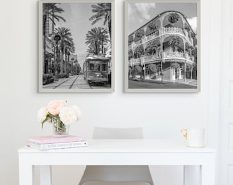 May include: Four framed black and white photographs of New Orleans scenes. One shows a street sign that reads "Orleans", another a church, a third a streetcar, and the last a building with a balcony. The photos are displayed above a white desk.