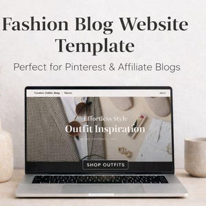 May include: A laptop displays a fashion blog website template with the text "Fashion Blog Website Template" and "Outfit Inspiration." A beige vase with dried pampas grass and a beige mug are on the table.