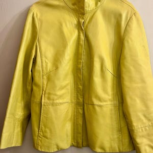 May include: A bright yellow leather jacket with a stand-up collar. The jacket has a tailored fit with seams and panels, and a single-button closure. The sleeves are long, and the jacket appears to be in good condition.