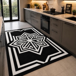 Può includere: Tappeto geometrico bianco e nero con motivo a stella. Il tappeto rettangolare è posto in una cucina. Il design presenta audaci linee bianche su sfondo nero. Il tappeto è lungo circa 180 cm.