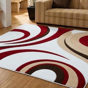 Può includere: Un tappeto rettangolare con sfondo bianco e grandi motivi circolari e curvi in tonalità rosso intenso, marrone scuro e beige. Il design è composto da archi sovrapposti che creano un flusso visivo audace e ritmico sull'intera superficie del rivestimento per pavimenti.