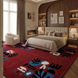 Può includere: Un grande tappeto rettangolare con uno sfondo rosso intenso e forme organiche astratte in nero, blu e bianco. Il tappeto copre una parte significativa del pavimento della camera da letto, estendendosi dai piedi del letto verso il primo piano.
