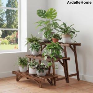 May include: A wooden plant stand with three tiers, holding various potted plants. The stand is made of dark brown wood and is positioned in front of a window. The plants include ferns and leafy green plants.