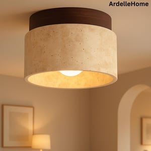 May include: A modern ceiling light fixture with a cylindrical shade. The light has a dark brown top and a beige, speckled shade. The text "ArdelleHome" is in the upper right corner. The light fixture is illuminated with a warm, soft glow.