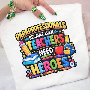 May include: White t-shirt with a colorful graphic that reads "PARAPROFESSIONALS BECAUSE EVEN TEACHERS NEED HEROES." The design includes a pencil, books, an apple, a backpack, and crayons.