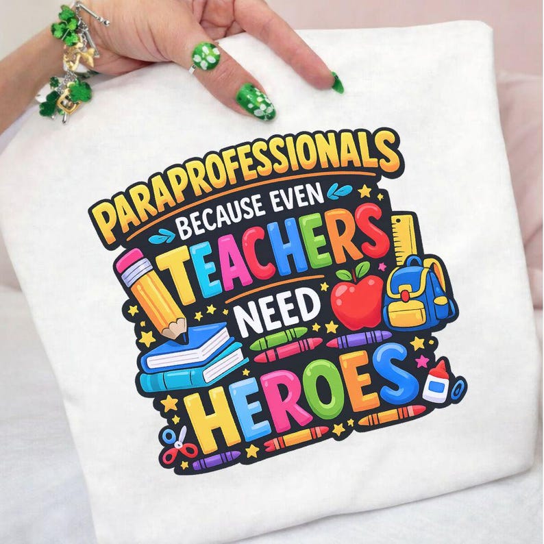 May include: White t-shirt with a colorful graphic that reads "PARAPROFESSIONALS BECAUSE EVEN TEACHERS NEED HEROES." The design includes a pencil, books, an apple, a backpack, and crayons.