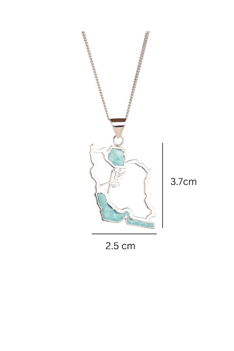 May include: A silver-colored necklace with a pendant shaped like the outline of a country, filled with turquoise-colored stone. The pendant is 2.5 cm wide and 3.7 cm tall. The necklace is on a white background.