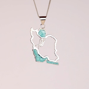 May include: Silver-toned pendant necklace featuring the outline of a country, filled with turquoise-colored stone. The pendant hangs from a delicate chain, creating a simple yet elegant design. The necklace is a unique piece of jewelry.