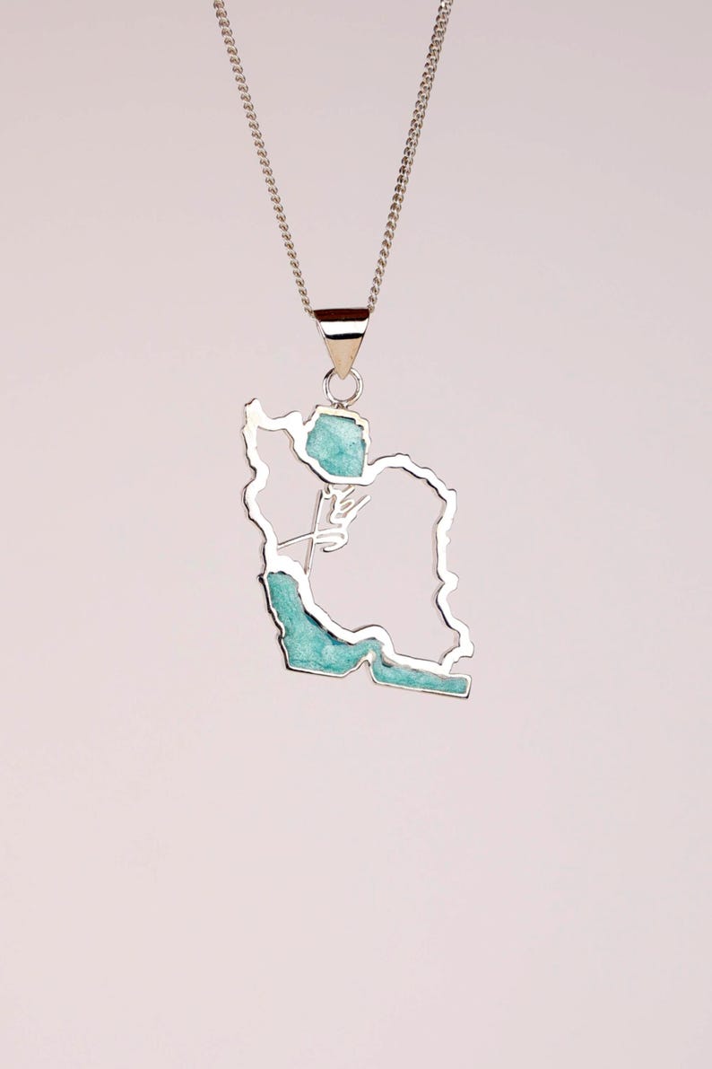 May include: Silver-toned pendant necklace featuring the outline of a country, filled with turquoise-colored stone. The pendant hangs from a delicate chain, creating a simple yet elegant design. The necklace is a unique piece of jewelry.