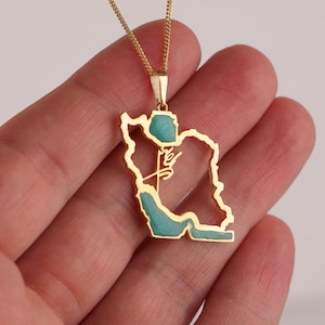 May include: A gold-colored pendant necklace featuring the outline of a country, with turquoise-colored accents. The pendant is suspended from a delicate gold chain. The necklace is a piece of jewelry.