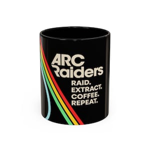 Puede incluir: Taza de cerámica negra con el texto "ARC Raiders" y "RAID. EXTRACT. COFFEE. REPEAT." en blanco. Un diseño de arcoíris colorido en rojo, amarillo, verde y azul recorre el lateral de la taza.