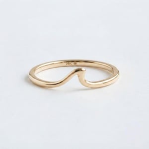 Könnte beinhalten: Ein goldener Ring mit einem wellenförmigen Design entlang der Ringschiene. Auf der Innenseite ist deutlich der Text 14K gefolgt von einem kleinen Sternsymbol eingraviert. Der Ring hat eine polierte, glatte metallische Oberfläche und eine runde Form.