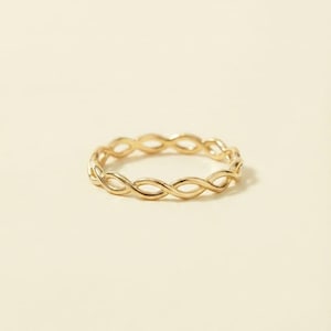 Op de afbeelding: Een dunne gouden ring met een doorlopend gedraaid of gevlochten ontwerp. De band is gemaakt van gepolijst geel metaal en vormt een reeks kleine, met elkaar verbonden ovale lussen die een delicaat, uniform patroon rond de hele omtrek vormen.
