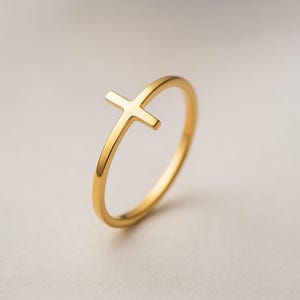 以下が含まれることがあります： シンプルな十字架のデザインが施されたゴールドカラーのリング。リングは細いバンドと、上部に小さな隆起した十字架が付いています。リングは光沢のある反射性の金属で作られています。リングのサイズはミリメートルで測定されます。