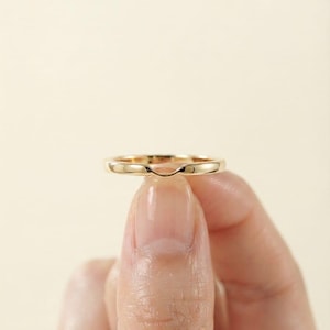 Pode incluir: Um anel de ouro amarelo polido com uma banda lisa e contínua, apresentando uma sutil depressão ou contorno arredondado ao longo da borda superior. O metal tem um acabamento reflexivo e brilhante, exibindo um design simples e limpo que se curva.