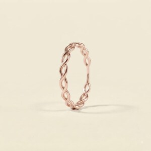 Puede incluir: Un anillo de oro rosa que presenta un diseño continuo de cuerda trenzada o estilo infinito. La banda está compuesta por bucles ovalados interconectados que crean un patrón repetitivo alrededor de toda la circunferencia de la joya circular.