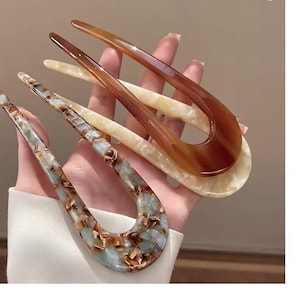 Könnte beinhalten: Drei dekorative Haargabeln in Braun-, Creme- und Blaugrüntönen. Die Haaraccessoires bestehen aus einem marmorierten Material und haben ein U-förmiges Design. Der Text "CREATION FRANCE" ist auf einer der Gabeln zu sehen.