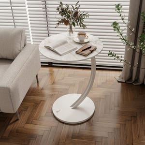 Könnte beinhalten: Ein weißer Beistelltisch mit Marmor-Effekt-Platte, getragen von einem gebogenen weißen Metallbein und einem kreisförmigen Sockel. Auf dem Tisch liegen ein offenes Buch, eine Tasse Tee und ein Notizbuch. Der Tisch hat einen Durchmesser von ca. 61 cm.