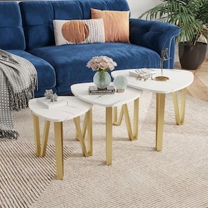 May include: A trio of nesting tables with white marble-effect tops and gold metal legs. The tables are triangular, varying in size, and arranged on a neutral rug. The tables are in front of a blue sofa.