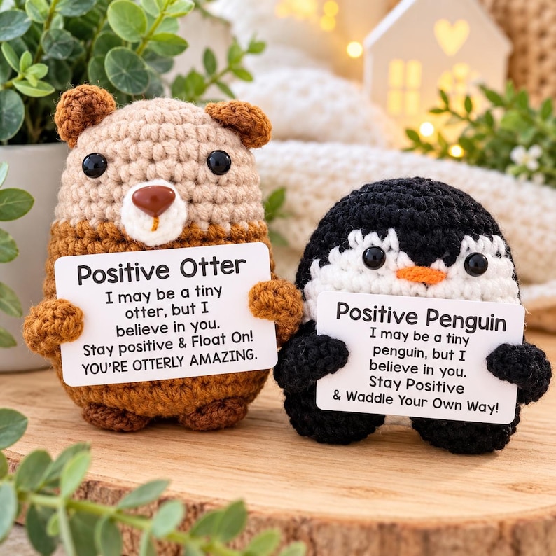 May include: Two crocheted stuffed animals, a tan otter and a black and white penguin, each holding a white card. The otter card reads: Positive Otter, I may be a tiny otter, but I believe in you. Stay positive & Float On! YOU'RE OTTERLY AMAZING.