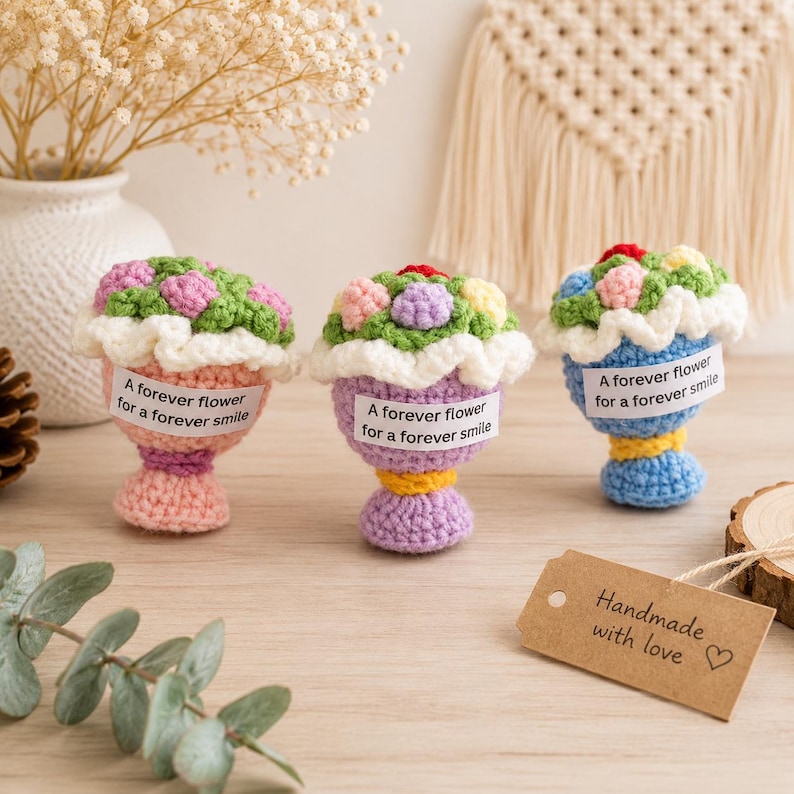 May include: Three small crocheted flower bouquets in pink, purple, and blue pots. Each bouquet features colorful yarn flowers with white ruffled edges and a white label printed with the text A forever flower for a forever smile.